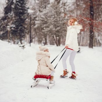 Family sleding in a winter park. Stylish mother in a red sweater. Little girl in a winter clothes.
